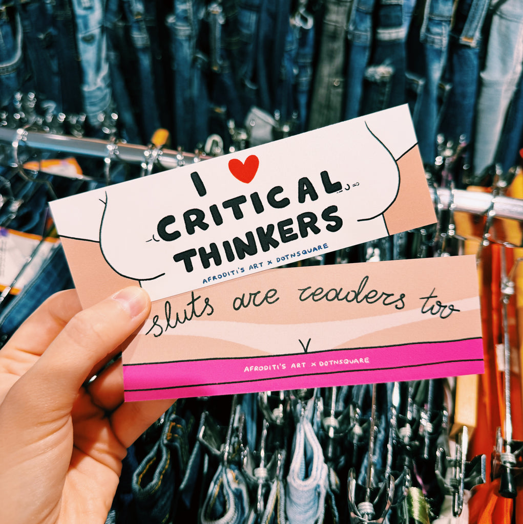 bookmark with text 'I ❤️ Critical Thinkers, Sluts are readers too' held in front of denim jeans.