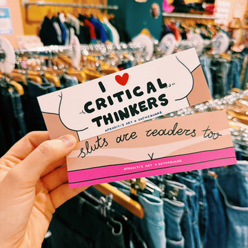 bookmark with text 'I ❤️ Critical Thinkers, sluts are readers too' held in front of a clothing store.