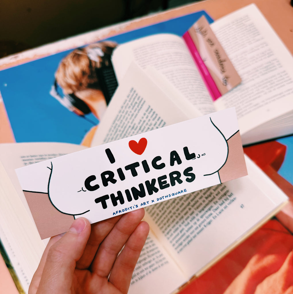 Hand holding a bookmark with 'I ❤️ Critical Thinkers' text over an open book.